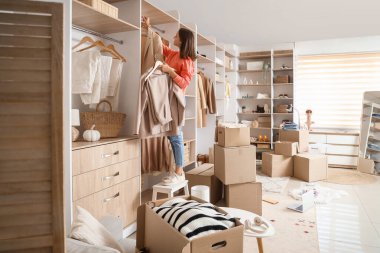 Young woman taking clothes from rack with wardrobe boxes in dressing room
