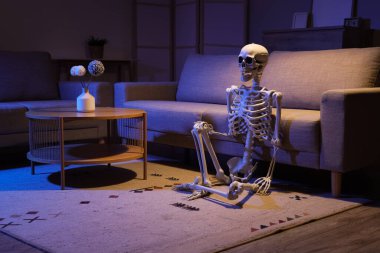 Human skeleton model on carpet near sofa in living room at night