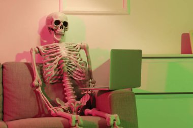 Human skeleton model with laptop on sofa in dark office