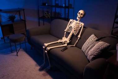 Human skeleton model sitting on sofa in dark living room