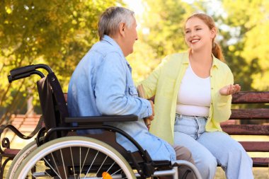 Senior woman in wheelchair with book and caregiver talking outdoors