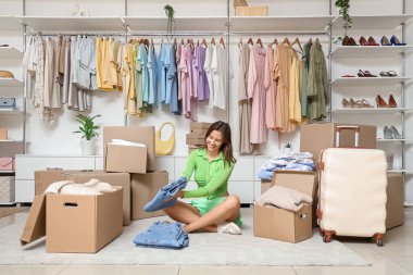 Young woman with folded jeans and wardrobe boxes sitting in dressing room