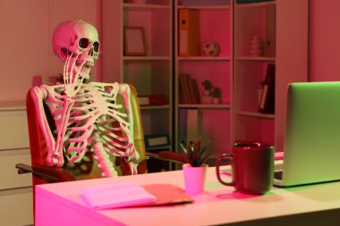 İnsan iskeleti modeli karanlık ofiste masa başında sohbet ediyor.