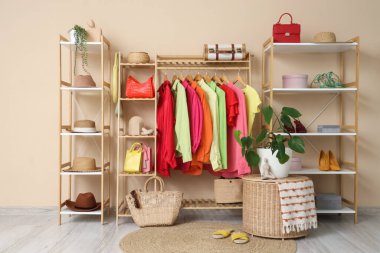 Giysi askısı ve raf üniteleri, soyunma odasındaki bej duvarın yanında aksesuarlar.