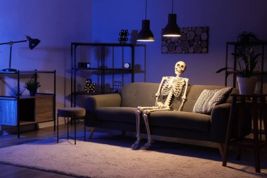 Human skeleton model sitting on sofa in dark living room