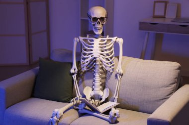 Human skeleton model with eyeglasses on sofa in dark living room