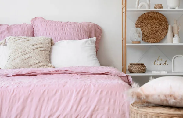 Bed with stylish pink bedding, shelving unit and home decor in bedroom