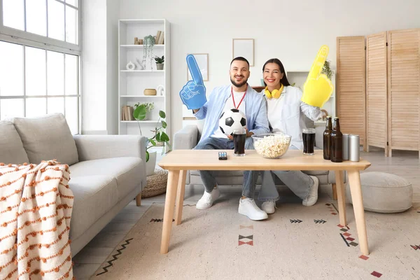 Köpüklü parmakları olan genç bir çift evdeki kanepede maç izliyor.
