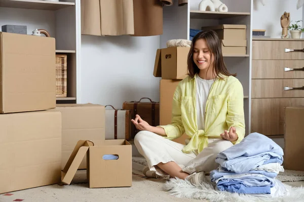 Young woman with wardrobe boxes meditating in dressing room
