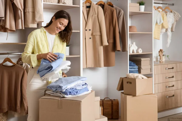 Young woman with folded clothes and wardrobe boxes in dressing room