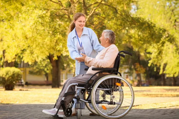 Young caregiver with senior woman in wheelchair talking outdoors
