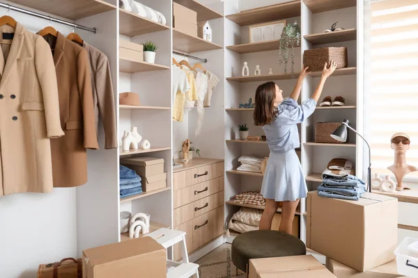 Young woman taking basket from shelf in wardrobe, back view