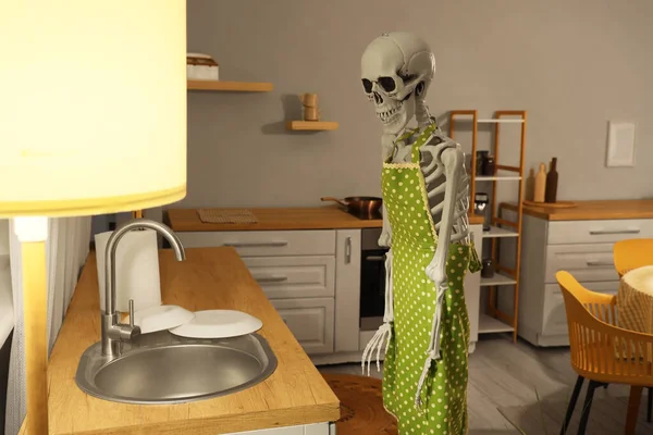 Human skeleton model with apron near sink in kitchen at night