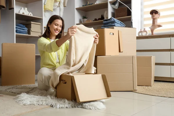Young woman with sweater and wardrobe boxes sitting in dressing room