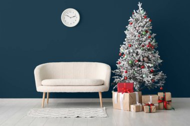 Yeşil duvara karşı hediyeler ve kanepe ile süslenmiş Noel ağacı.