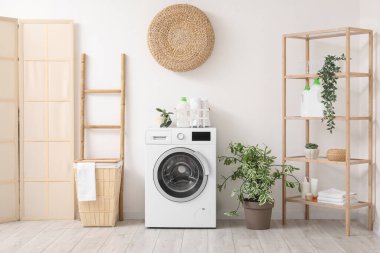 Sepeti, raf ünitesi ve beyaz duvarın yanındaki merdiveni olan modern çamaşır makinesi. Ev çamaşır odasının içi.