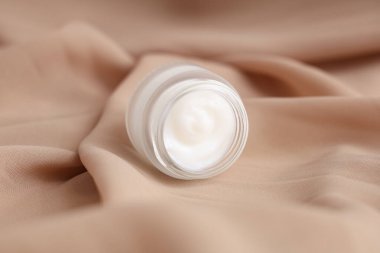 Arka plan olarak bej kumaş üzerine kozmetik ürünü olan kavanoz, yakın plan