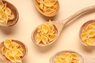 Bej arka planda çiğ makarna kabuklu tahta kaşıklar.