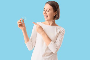 Young woman pointing at occlusal splint on blue background