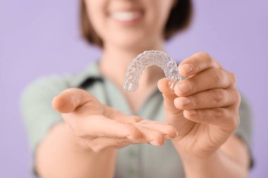 Young woman with occlusal splint on lilac background, closeup