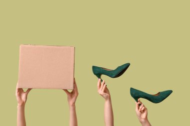 Female hands with wardrobe box and high heels on green background