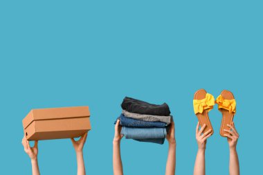 Female hands with wardrobe box, jeans and shoes on blue background