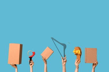 Female hands with wardrobe boxes, shoes, hanger and adhesive tape on blue background