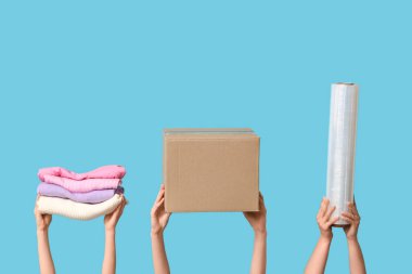 Female hands with wardrobe box, clothes and stretch wrap on blue background