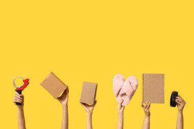 Female hands with wardrobe boxes, slippers, belt and adhesive tape on yellow background