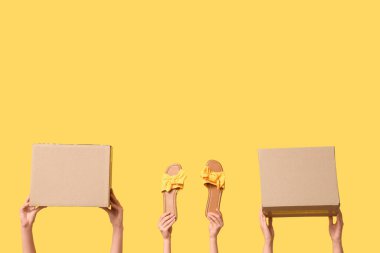 Female hands with wardrobe boxes and shoes on yellow background