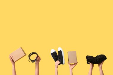 Female hands with wardrobe boxes and accessories on yellow background