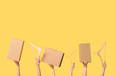 Female hands with wardrobe boxes and hangers on yellow background