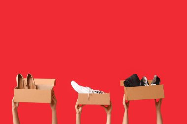 Kadın eli, kırmızı arka planda spor ayakkabılı ve elbiseli gardırop kutularını tutuyor.