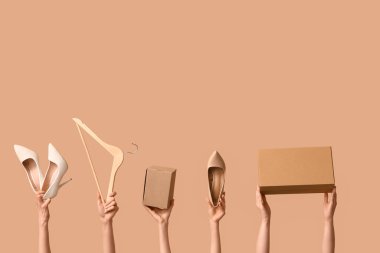 Female hands with wardrobe boxes, high heels and hanger on beige background