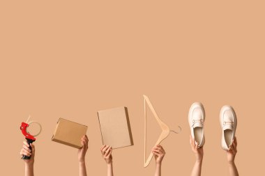 Female hands with wardrobe boxes, hanger, shoes and adhesive tape on beige background