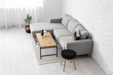 Interior of light living room with grey sofa, table and stool