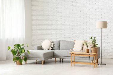 Gri kanepe, masa ve bitkilerle aydınlık oturma odasının içinde.