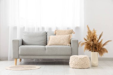 Aydınlık oturma odasının içinde gri kanepe, puf ve vazoda otlar.