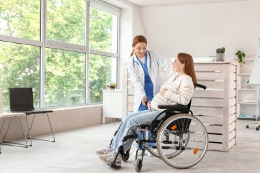 Young pregnant woman in wheelchair with doctor at hospital