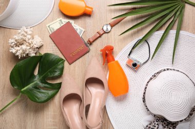 Female traveler's accessories with palm leaves on wooden floor, top view