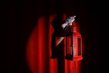 Female hand with lantern behind red curtain