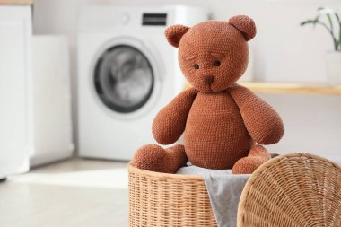 Wicker basket with toy bear in laundry room, closeup