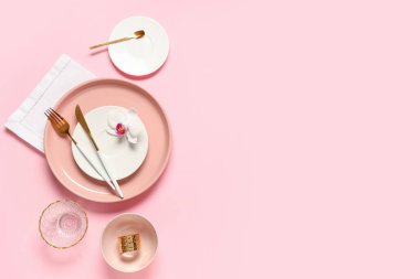Altın çatal bıçak takımı ve pembe arka planda orkide çiçeğiyle güzel bir masa.