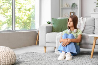 Sad teenage girl sitting on carpet at home