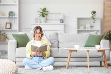 Evde halıda kitap okuyan güzel bir kadın.