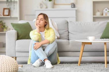 Sad young woman sitting on carpet at home
