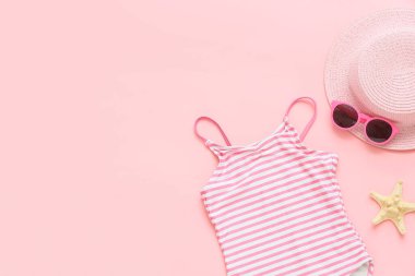 Children's swimsuit with sunglasses, hat and starfish on pink background