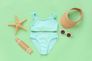 Yeşil arka planda plaj aksesuarları olan çocuk mayosu.