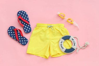 Çocuk yüzme şortu ve pembe arka planda plaj aksesuarları.