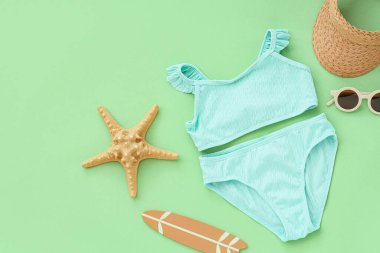 Yeşil arka planda plaj aksesuarları olan çocuk mayosu.